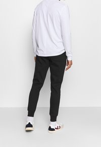 Witte lange mouwen blouse met een ronde hals, gecombineerd met zwarte tapered joggingbroek en meerkleurige lage sneakers.