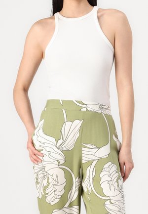 Kvinde iført hvid ærmeløs ribbet halterneck-top og olivengrønne bukser med højtalje og stort hvidt blomsterprint.