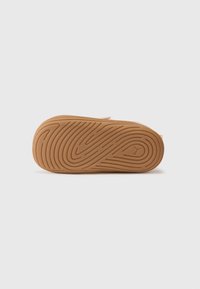 Semelle en caoutchouc avec un motif texturé et ondulé en beige. Un petit logo est visible près du talon. La surface est lisse et légèrement brillante.