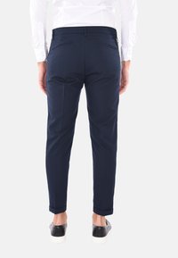 Pantaloni blu navy realizzati in un tessuto morbido, con una vestibilità slim, vita piatta e due tasche posteriori con zip. Orli a cuffia e scarpe casual.