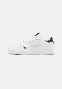 Hvide lædersneakers med perforerede sider, sorte detaljer på hælen og tungen samt et signaturlogo på siden. Gummisål.