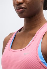 Εικόνα κοντινού πλάνου ενός ατόμου που φοράει ροζ αθλητική μπλούζα με ραβδώσεις πάνω από ανοιχτό μπλε αθλητικό σουτιέν, με ένα μικρό ασημί λογότυπο της Nike ορατό.