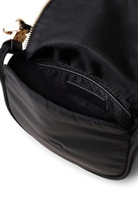 Interno di una borsa nera in pelle con fodera testurizzata, chiusura a zip e una tasca piccola etichettata con un logo. Hardware tono oro visibile.