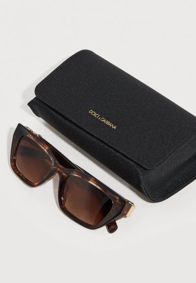 Ορθογώνια γυαλιά ηλίου με καφέ φακούς και καφέ-μαύρο σχέδιο κελύφους χελώνας δίπλα σε κλειστή μαύρη θήκη Dolce & Gabbana πάνω σε λευκή επιφάνεια.