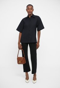 Camisa negra a rayas de manga corta, ajustada, con botones en el frente. Pantalones negros acampanados, tacones blancos de punta, bolso marrón cruzado con herrajes dorados.