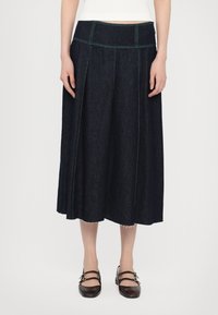 Mørk denim midiskjørt med grønn søm, med flat midjebånd og pregede detaljer. Kombinert med brune flate sko.
