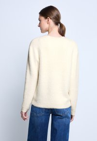 Cremfarbener, strukturierter Pullover mit langen Ärmeln und Rundhalsausschnitt, kombiniert mit blauen weit geschnittenen Jeans. Sichtbare Nähte und lockere Passform.