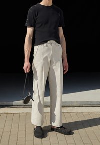 Sort ribbet T-shirt med korte ærmer, cremefarvede brede bukser, sort rund taske med rem og sorte slip-on sko. Teksturdesign med moderne udtryk.