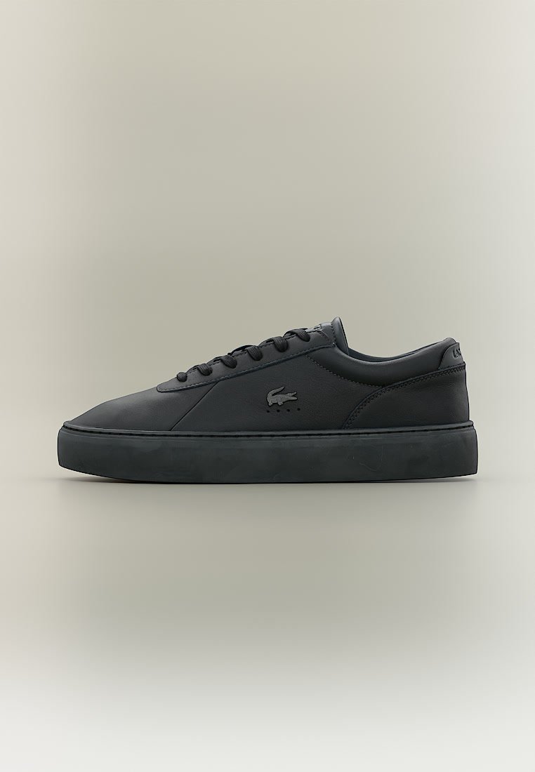 Черна ниска спортна обувка с връзки, дебела подметка и логото на крокодила на Lacoste отстрани, показана в профил на неутрален фон.