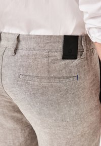 Gray linen pants with a textured finish, featuring a black brand tag and a small blue accent stitch on the back pocket.