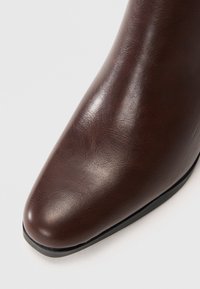 Brune lær ankelsko med spiss tå, glatt tekstur og et strømlinjeformet design. Har en flat svart såle. Ingen synlige detaljer eller pynt.