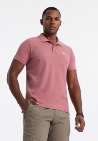 Lyhythihainen polo-paita vaaleanpunaisesta puuvillasta, jossa on kaulus ja brodeerattu logo. Yhdistetty beigenvärisiin cargo-shortseihin, joissa on vetoketjulliset taskut.