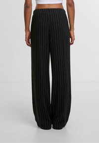 Čierne široké nohavice s bielymi prúžkami, elastický pás a jemná textúra. Dizajn zahŕňa voľný strih a nohavice v plnej dĺžke.