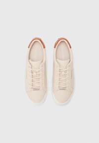 Sneaker beige di Calvin Klein con design a lacci, tessuto morbido e dettagli in suede marrone sul tallone. Suole in gomma bianca e branding minimale.