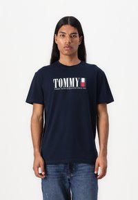 Navyblauwe katoenen t-shirt met een wit "TOMMY" logo en een Franse vlagaccent. Relaxed fit met korte mouwen en een ronde hals.