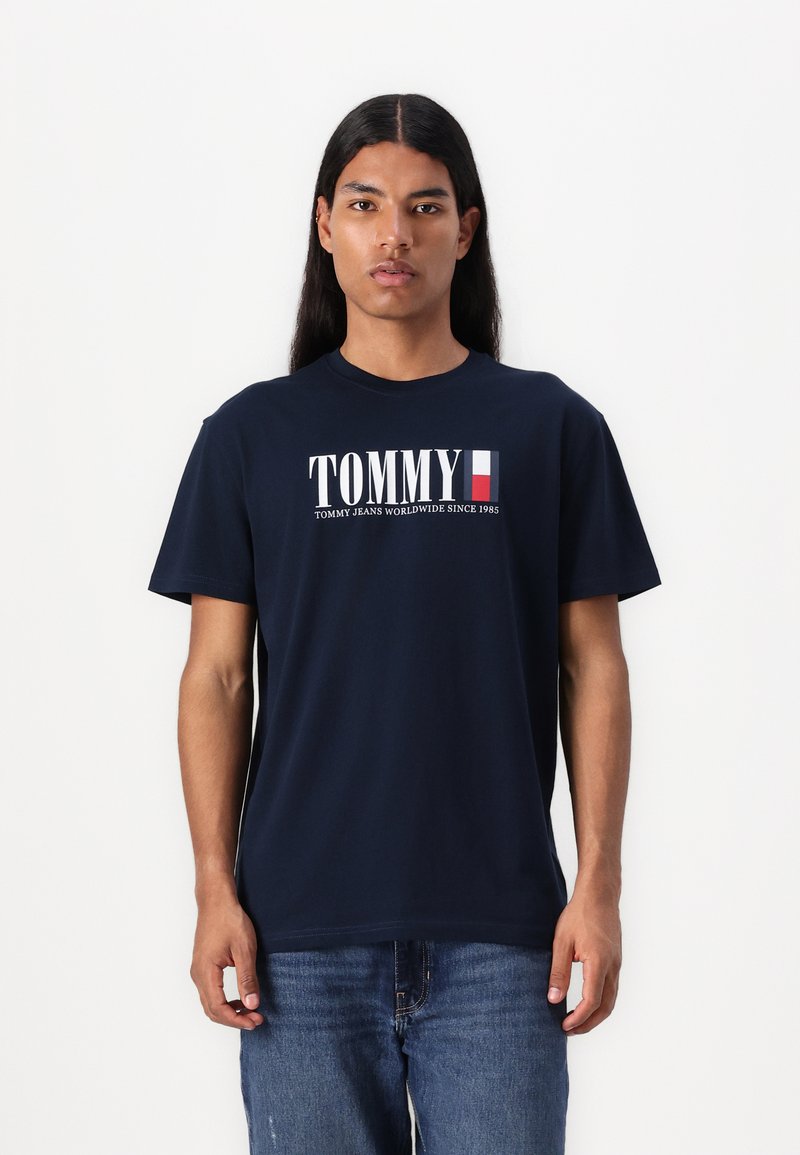 Navyblauwe katoenen t-shirt met een wit "TOMMY" logo en een Franse vlagaccent. Relaxed fit met korte mouwen en een ronde hals.