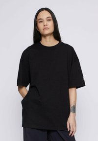Camiseta negra de gran tamaño hecha de algodón. Presenta un cuello redondo, mangas cortas y un pequeño logo de la marca en la manga izquierda.