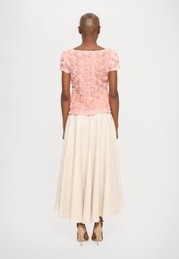 Haut à manches courtes, en rose avec une texture florale, associé à une jupe crème de longueur maximum. Un tissu lisse et des talons hauts neutres complètent le look.