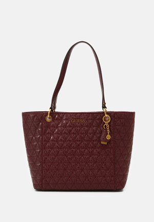 Sac cabas Guess bordeaux avec motif matelassé, logo doré et breloque, et deux bretelles sur fond blanc.