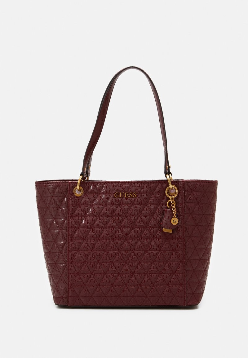 Sac cabas Guess bordeaux avec motif matelassé, logo doré et breloque, et deux bretelles sur fond blanc.