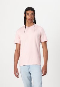 Helles rosa Baumwoll-T-Shirt mit kurzen Ärmeln und rundem Halsausschnitt, kombiniert mit hellblauen Jeans. Geschmeidige Textur, lässiger Schnitt.