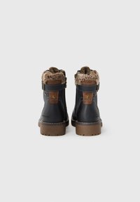 Bottes de cheville en cuir noir avec doublure en fourrure, accents bruns, sangles à boucle et semelles robustes brunes, vues de l'arrière sur un fond blanc.