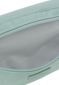 Pencil case v mátově zelené barvě s texturovaným povrchem, zipovým uzavíráním a hladkým šedým interiérem. V jedné části je umístěná štítek.