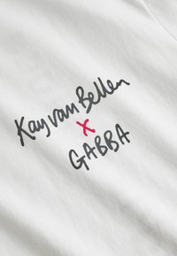 Tricou alb din bumbac cu text negru scris de mână "Kay van Bellen" și un "x" roșu, având "GABBA" în negru dedesubt. Textură moale, design casual.