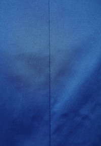 Modrá látka s hladkou texturou a mírným leskem. Má šev probíhající svisle uprostřed, což naznačuje upravený design.