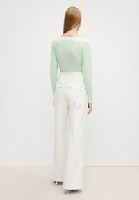 Blusa lunga a maniche trasparenti color menta abbinata a pantaloni bianchi a gamba larga con tasche posteriori e una trama liscia.