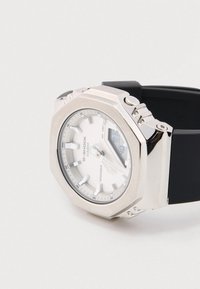 Hõbedase tooniga G-Shock käekell kaheksanurkse roostevabast terasest korpuse, valge sihverplaadi, musta kummirihma ja analoog-digitaalnäidikuga. Veekindel kuni 200 meetrit.