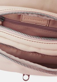 Interno di una borsa in pelle rosa chiaro con tre scomparti con cerniera e una texture liscia. Caratterizzata da hardware per cerniere di tonalità argento e un branding discreto.