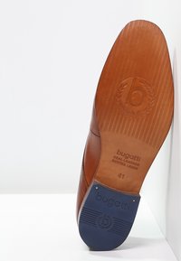 Semelle de chaussure habillée en cuir marron avec la marque "bugatti", taille 41, talon en caoutchouc texturé, et logo embossé sur une surface blanche.