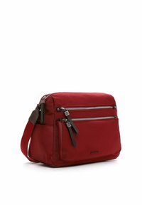 Punainen suorakaiteenmuotoinen olkalaukku, jossa säädettävä hihna, kaksi vaakasuoraa vetoketjutaskua ja etutasku läpällä valkoisella taustalla.