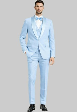 Homme portant un smoking bleu clair avec un nœud papillon assorti, une chemise blanche et des chaussures noires, debout avec une main dans la poche.