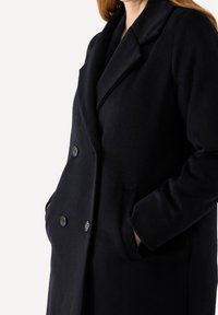 Cappotto in misto lana blu navy con design doppiopetto, colletto a rever, due tasche anteriori e bottoni neri.