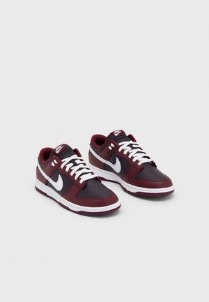 Par lavtop Nike-sneakers i mørkerød, sort og hvid med hvide snørebånd og Nike Swoosh-logoer på siderne.