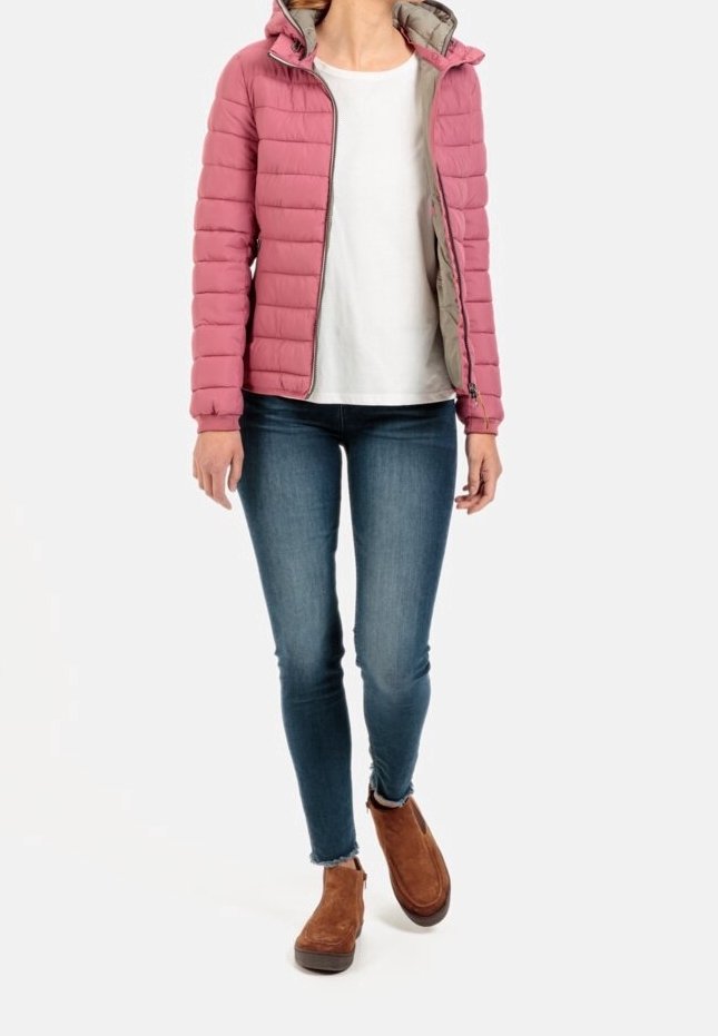 Personne portant une doudoune rose sur une chemise blanche, un jean skinny bleu et des bottines marron, debout avec un pied légèrement en avant.