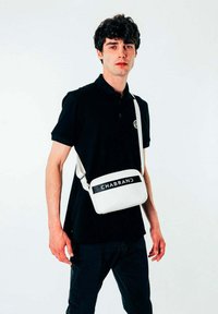 Borsa a tracolla bianca di forma rettangolare, con una tracolla nera e la parola "CHABRAND" in caratteri grassetto sulla parte anteriore.