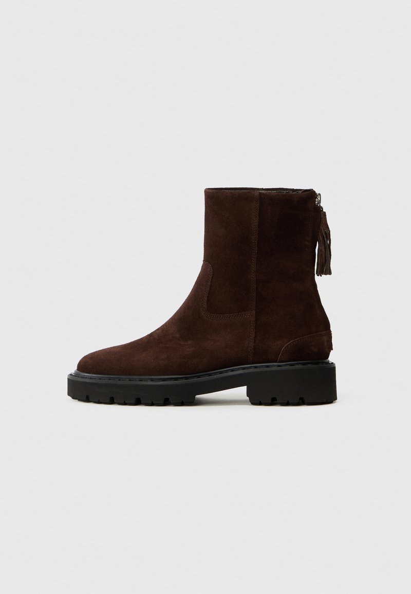 Botină din suede maro cu talpă din cauciuc negru, având un fermoar pe lateral și un detaliu cu ciucure. Textură netedă și design minimalist.