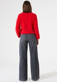 Roter, flauschiger Pullover mit langen Ärmeln, kombiniert mit weit geschnittenen, dunkelgrauen Jeans. Der Pullover hat einen runden Ausschnitt und einen lockeren Schnitt.