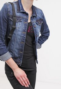 Džínová bunda v tmavě modré barvě s světle modrými manžetami, dvěma náprsními kapsami a kovovými knoflíky. Nositá přes černý top a spárovaná s černými kalhotami.