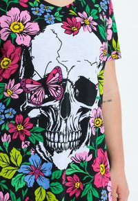 Black fabric t-shirt featuring a white skull graphic adorned with colorful flowers in pink, blue, and green, and a pink butterfly accent.