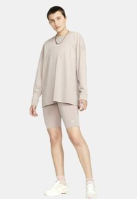 Långärmad ljusbeige topp i kombination med matchande beige cykelbyxor. Slätt tyg med avslappnad passform; har en liten Nike-logotyp.