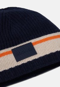 Pletená čepice v námořnické modré a krémové barvě s oranžovým pruhem. Má strukturovaný pletený design a obdélníkovou černou nálepku s vyraženým nápisem "BOGNER".
