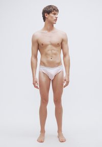 Ροζ βαμβακερά εσώρουχα με γκρι ελαστική ζώνη στη μέση, με λεία υφή και εφαρμοστό σχέδιο, που φοριούνται από έναν όρθιο ανδρικό φιγουρα.