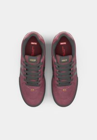 Burgundy suede sneakers with gray laces and accents, featuring a rounded toe and textured outsole. Gold logo detail on the tongue.