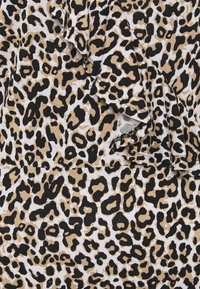 Tkanina w panterkę z czarnymi i brązowymi plamami na białym tle, z fakturowaną powierzchnią i falbaniastym wykończeniem.