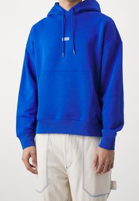 Felpa con cappuccio blu caratterizzata da una tasca anteriore, collo con cordoncino e dettaglio del logo. Realizzata in un tessuto morbido e strutturato.