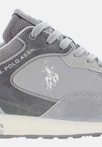 Scarpa sportiva grigia realizzata in materiali mesh e sintetici, con logo, dettagli testurizzati e un design di allacciatura classico.